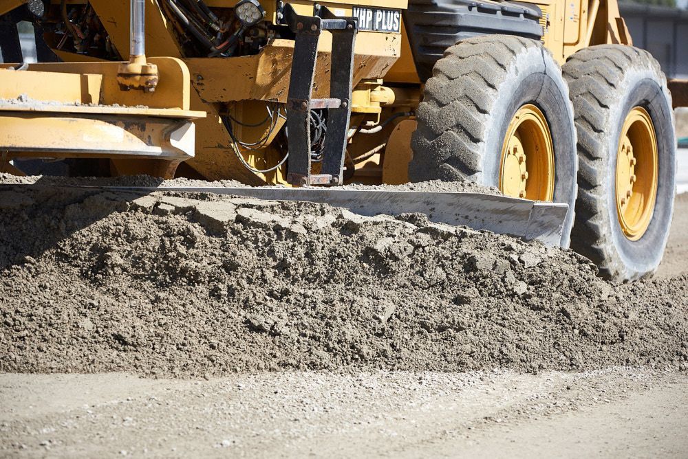 A Yellow Road Grader Blade Pushes a Large Pile of Dirt and Gravel — Quarrell Civil Construction In Congupna, VIC