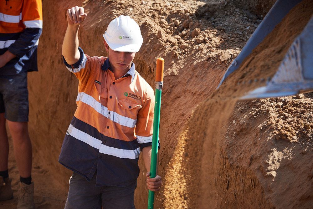Construction Worker In Orange Shirt And Hard Hat Holding A Shovel — Quarrell Civil Construction In Congupna, VIC