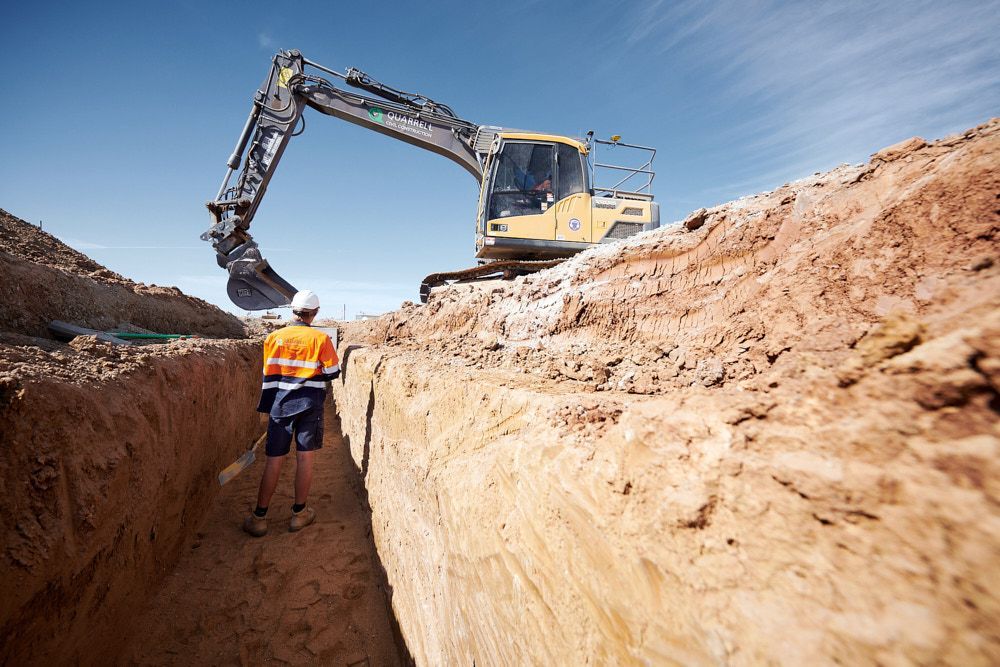 A Construction Worker in High-visibility Gear Stands in a Deep Dirt Trench — Quarrell Civil Construction In Congupna, VIC