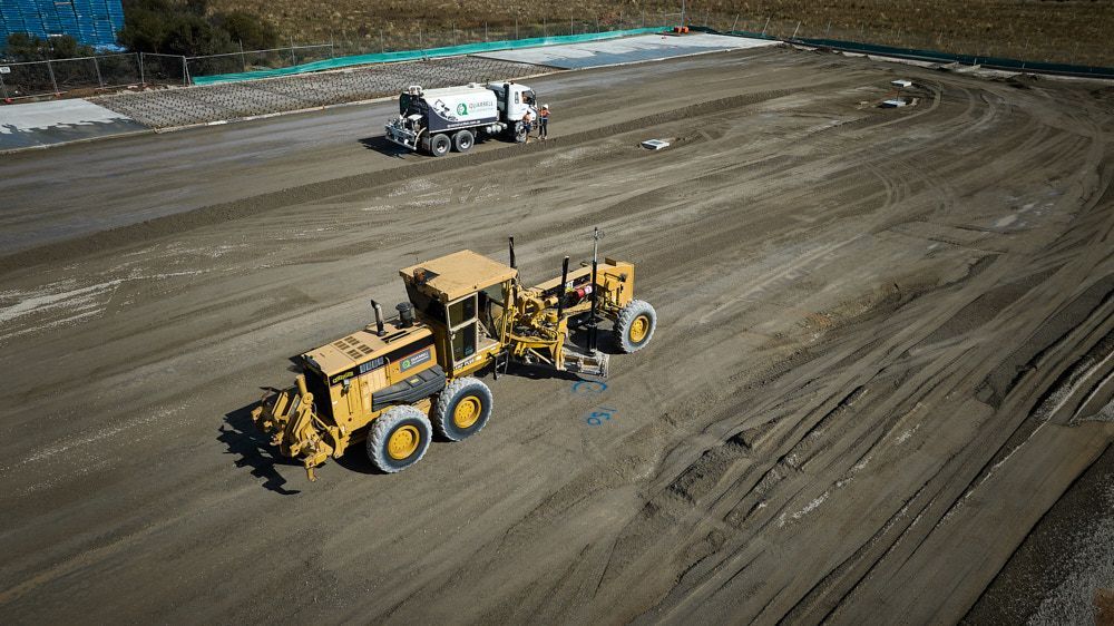 Yellow road grader smoothing dirt in construction site with a water truck in the background. — Quarrell Civil Construction In Congupna, VIC