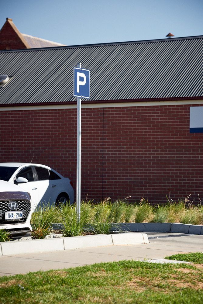 A Blue Parking Sign on a Silver Pole in Front of a Red Brick Building — Quarrell Civil Construction In Congupna, VIC