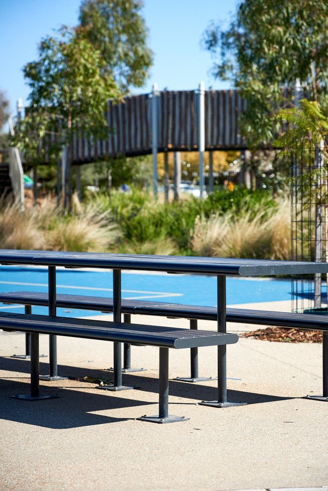 A Gray Metal Picnic Table Sits on a Paved Area in Front of a Blue Sports Court — Quarrell Civil Construction In Congupna, VIC