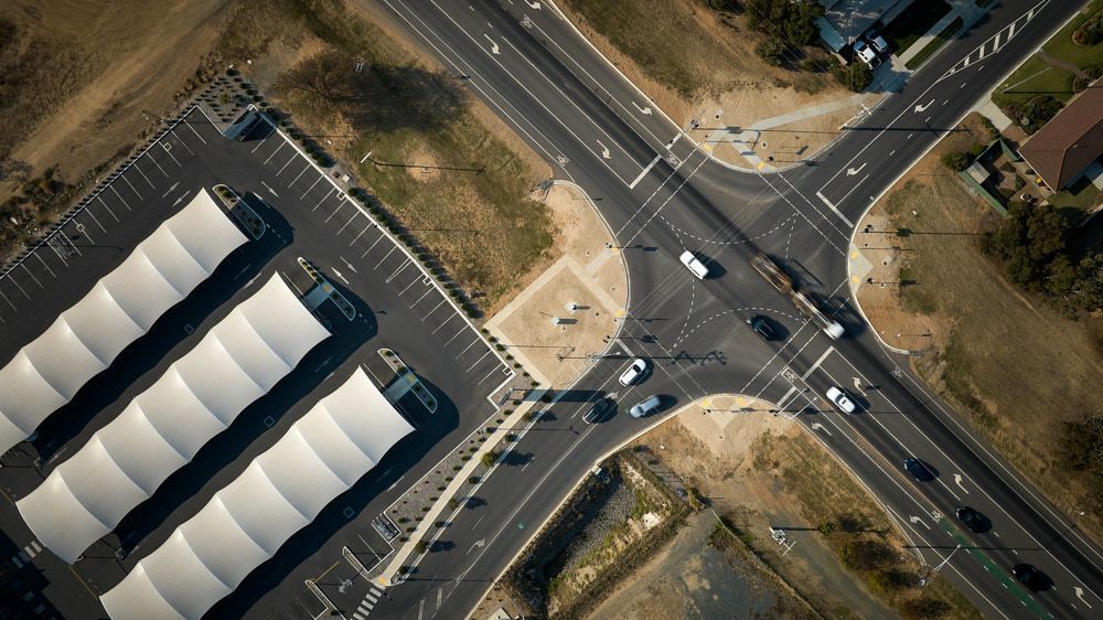 Aerial view of a road intersection beside a large parking lot with a long white-roofed building  — Quarrell Civil Construction In Congupna, VIC