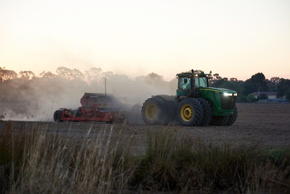 A Green John Deere Tractor Pulls a Red Seeder Across a Dusty Field — Quarrell Civil Construction In Congupna, VIC