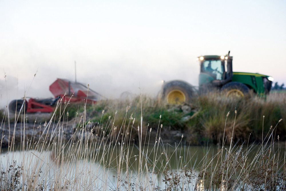 A Green Tractor Pulls Farm Equipment Through a Dusty Field — Quarrell Civil Construction In Congupna, VIC