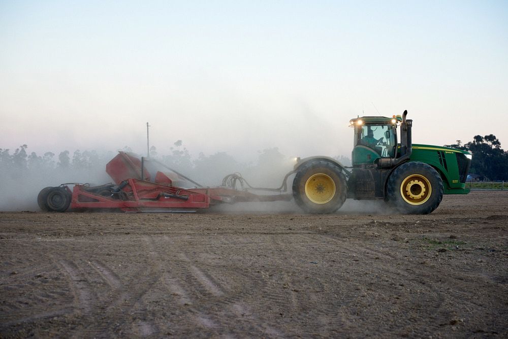A Green John Deere Tractor Pulls a Red Piece of Farm Equipment — Quarrell Civil Construction In Congupna, VIC