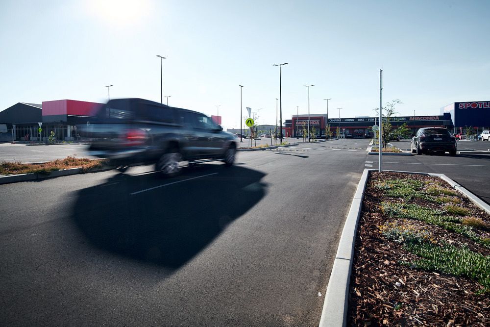 A Gray Vehicle Blurs as It Drives Through a Sunny Commercial Parking Lot — Quarrell Civil Construction In Congupna, VIC