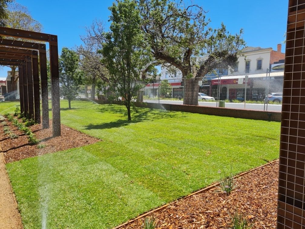A well-manicured lawn with trees and a wooden pergola is being watered by sprinklers in an urban park setting — Quarrell Civil Construction In Congupna, VIC