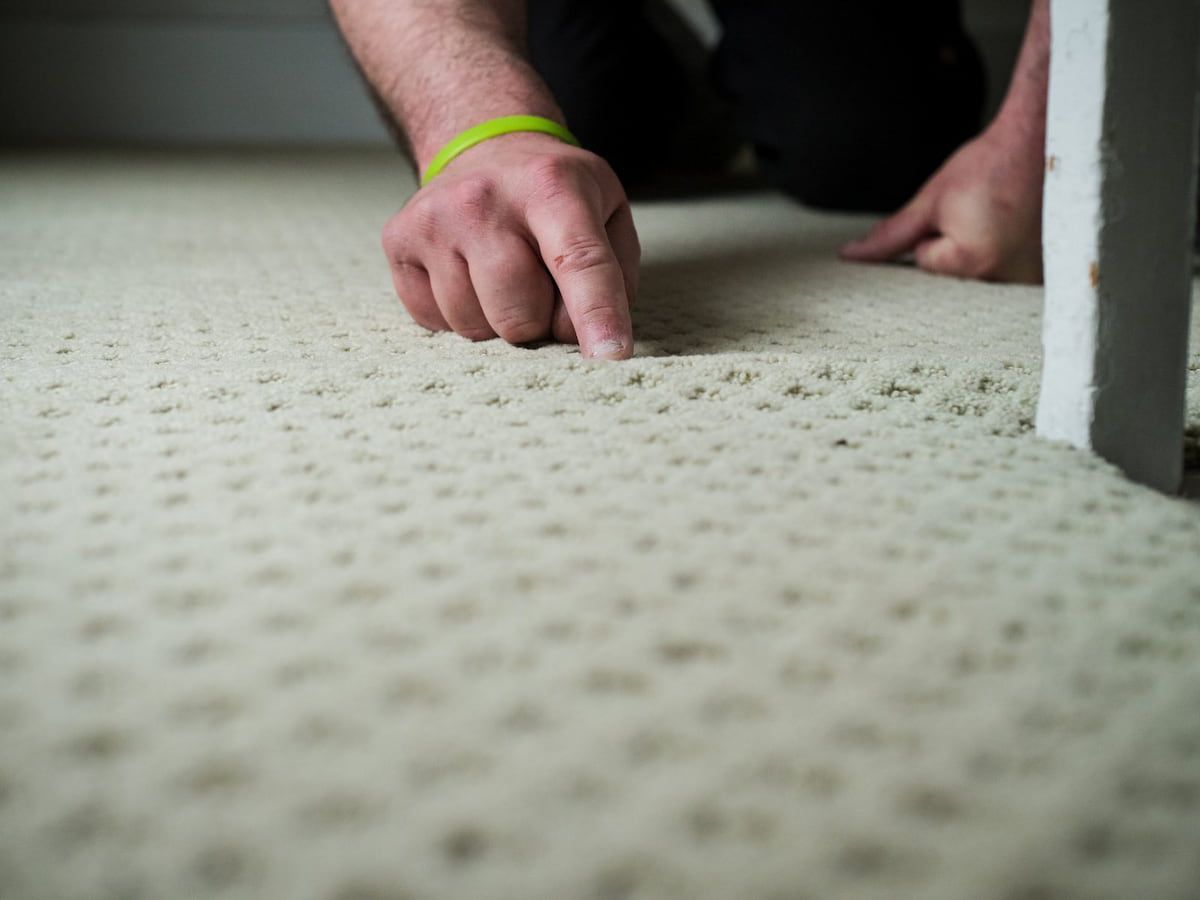 Hand pointing to the pile of a patterned carpet during a fiber inspection