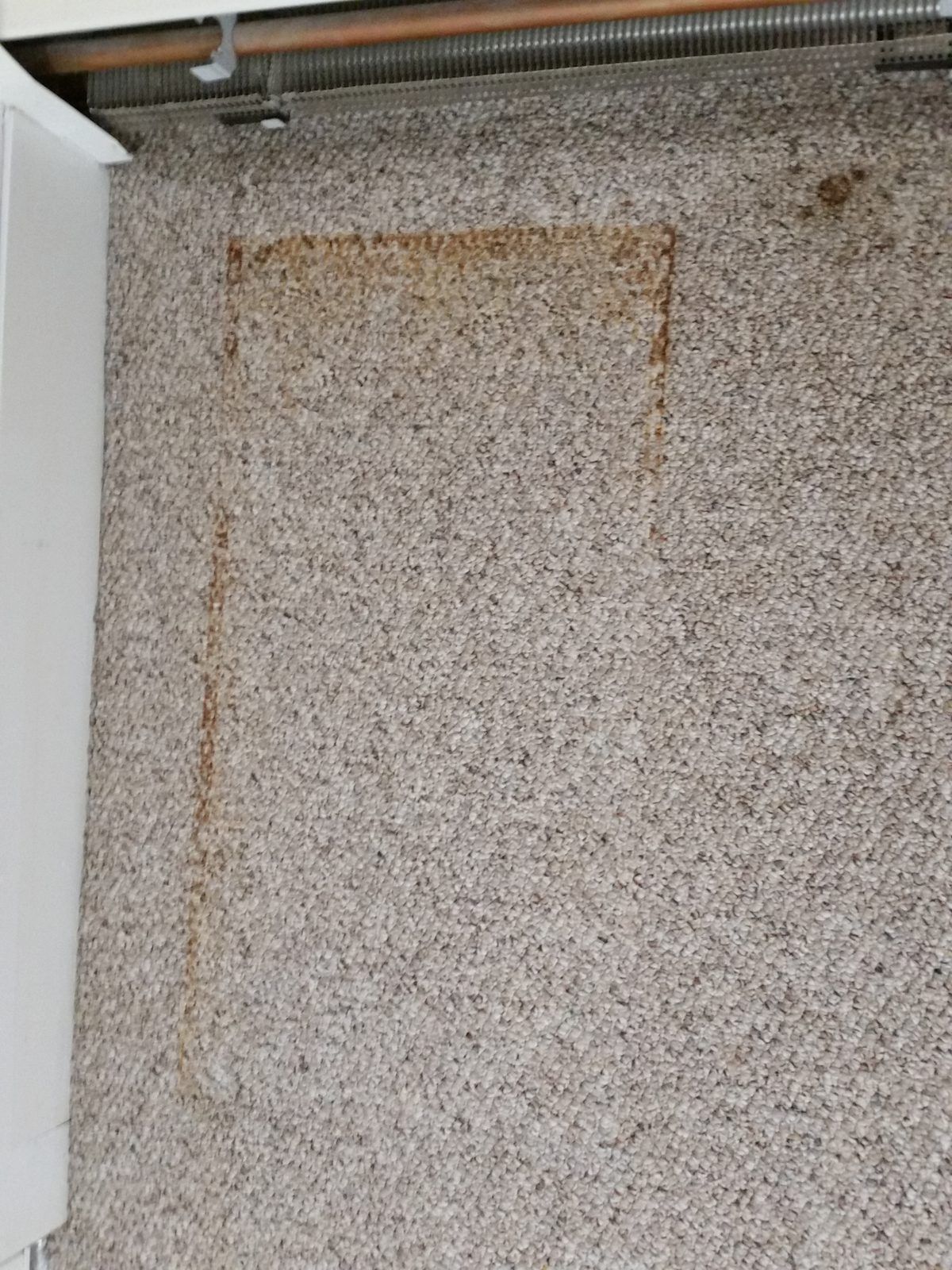 Beige loop-pile carpet with a rust-colored rectangular stain in the shape of an object that sat on it