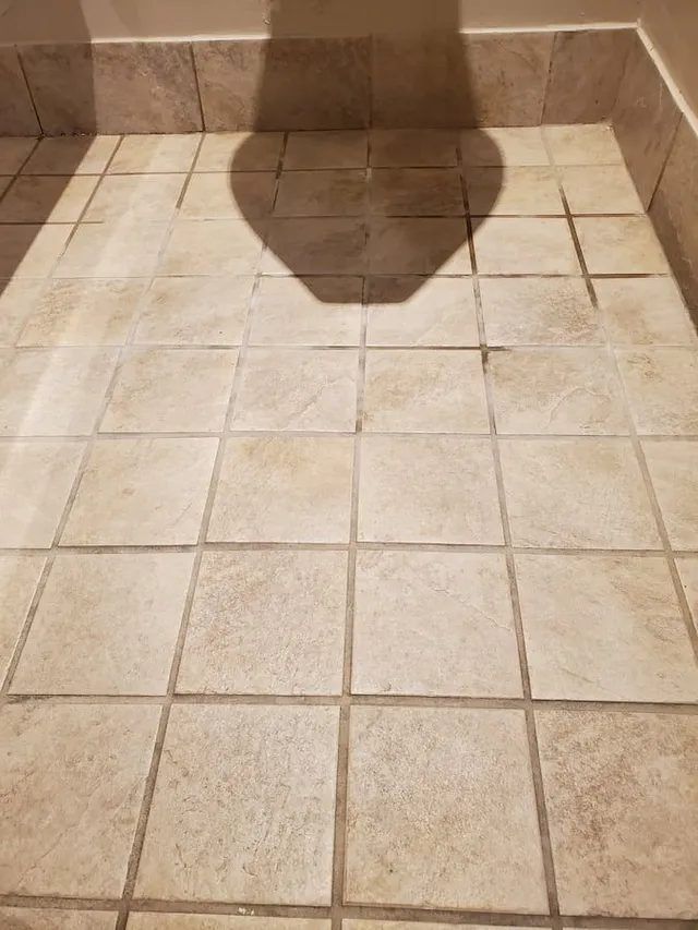 Office building men's restroom tile floor in front of a urinal with stained, darkened grout lines before cleaning