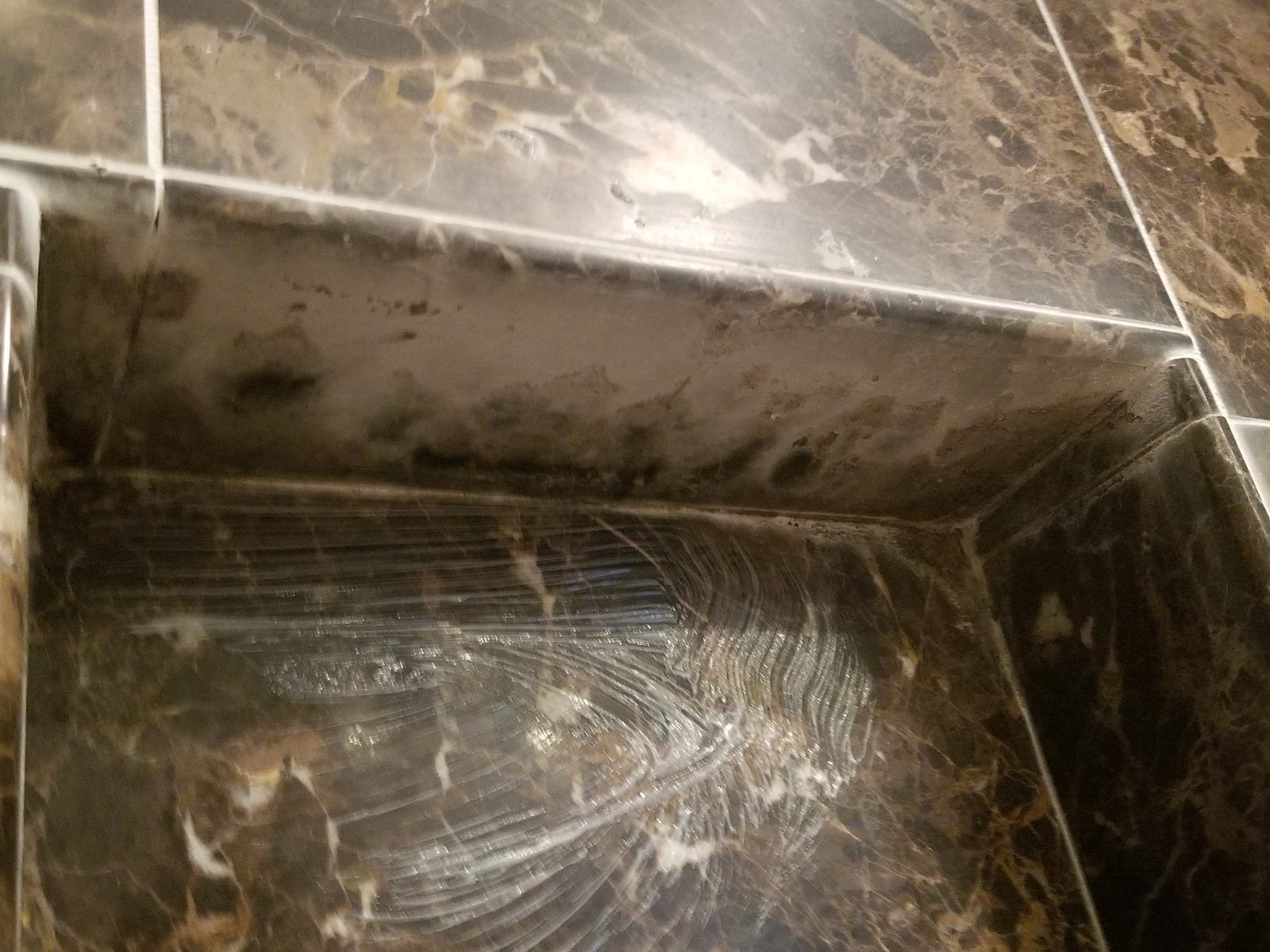 Dark brown marble shower corner covered in soap scum buildup before cleaning, Needham MA