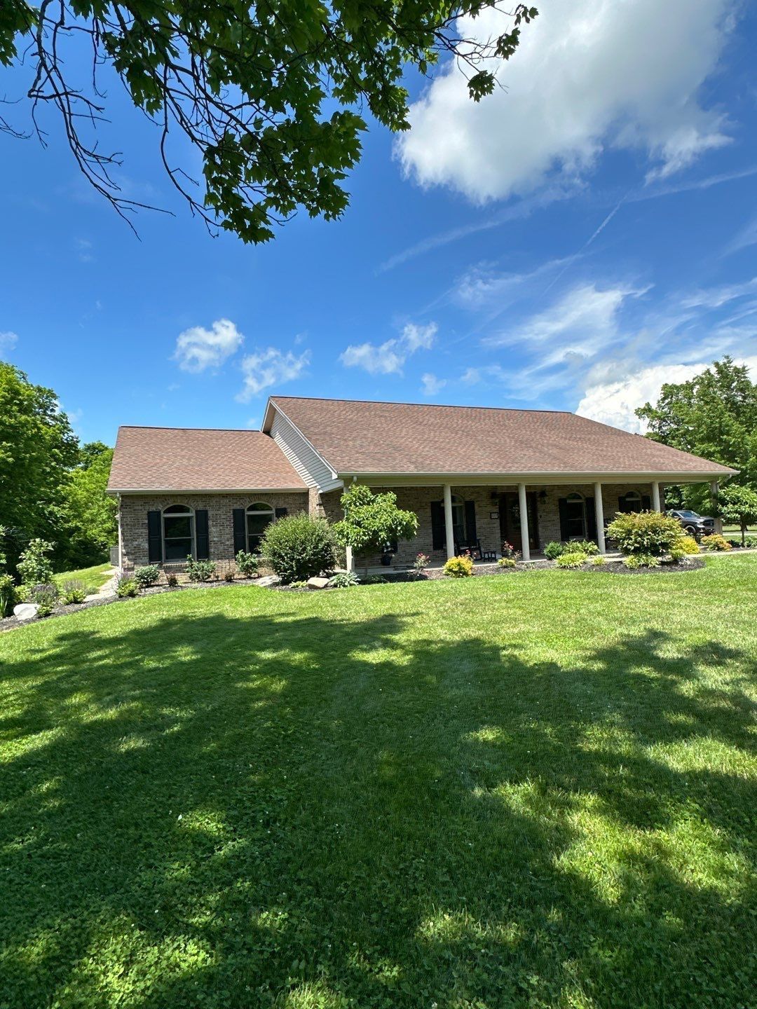 Backyard view of a brick house with a sloped roof, patio furniture, and a grassy lawn under a cloudy sky