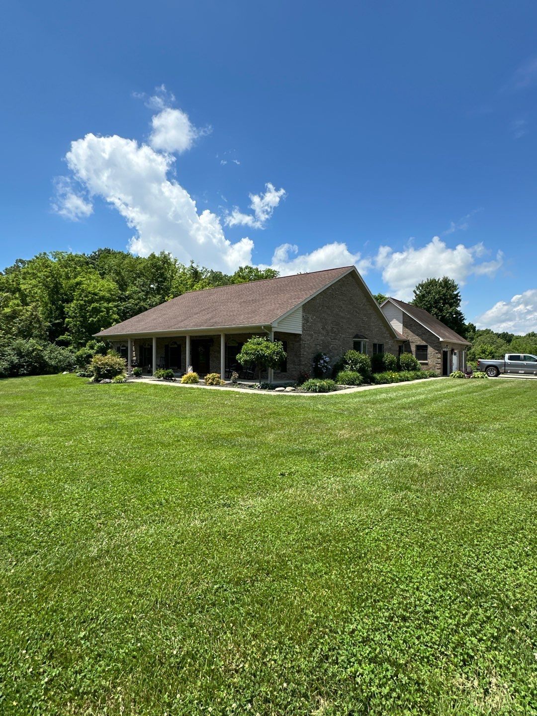 Backyard view of a brick house with a sloped roof, patio furniture, and a grassy lawn under a cloudy sky