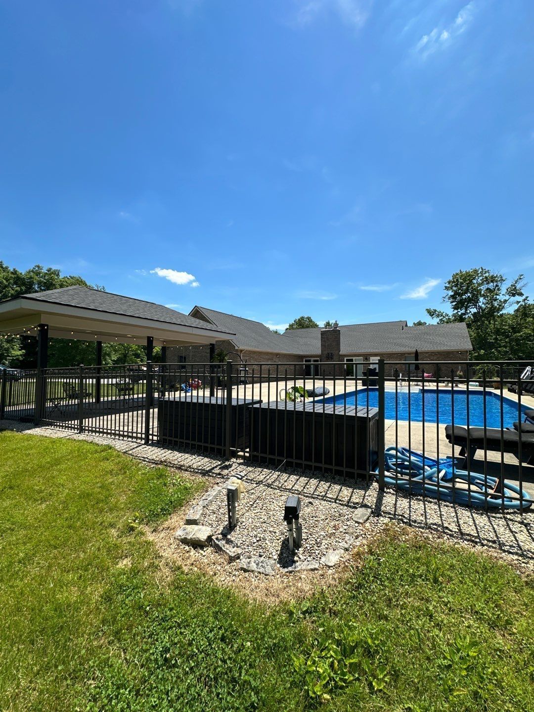 Backyard pool with black fence, patio umbrella, and bright blue sky