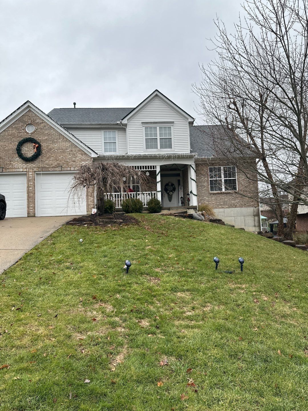 Suburban two-story house with a front lawn, white garage, and bare trees on an overcast day