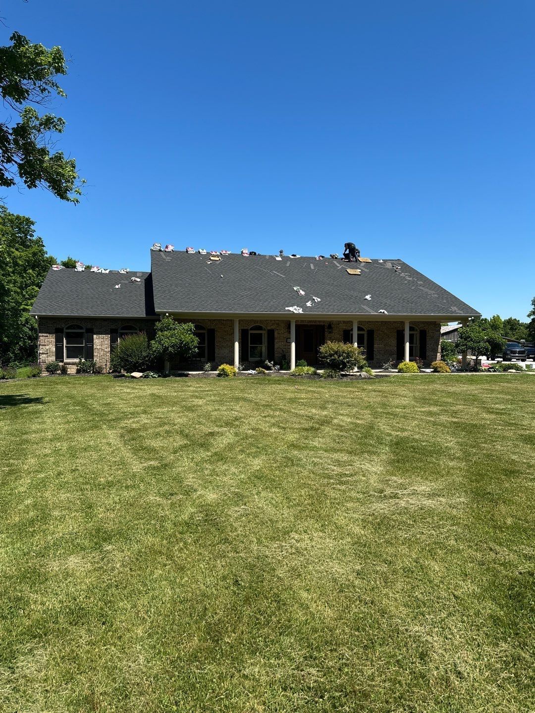 Single-story house with dark roof and porch, seen across a large mowed lawn under a clear blue sky