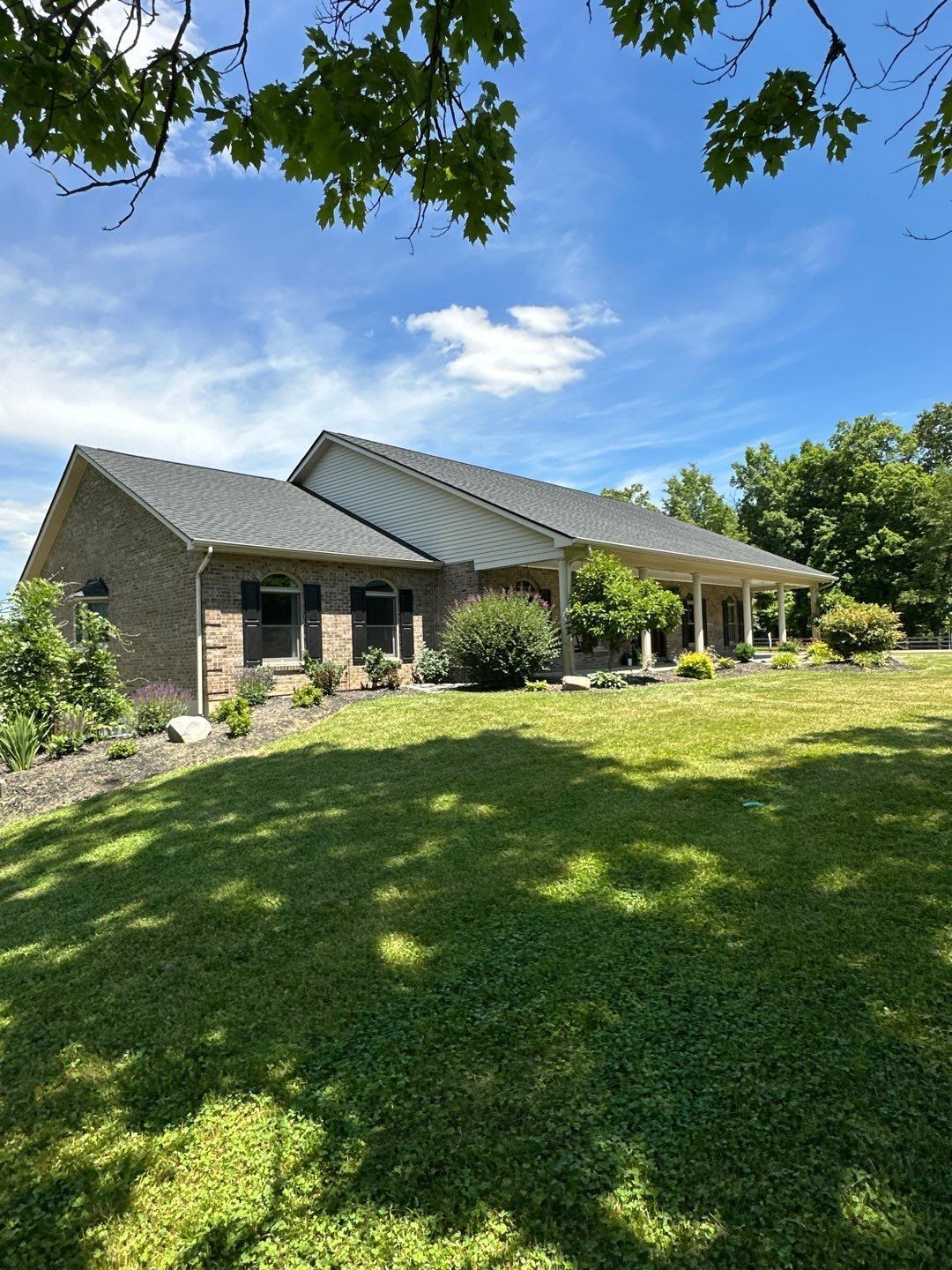 Brick house with a screened porch and metal roof, surrounded by a sunny green lawn and trees