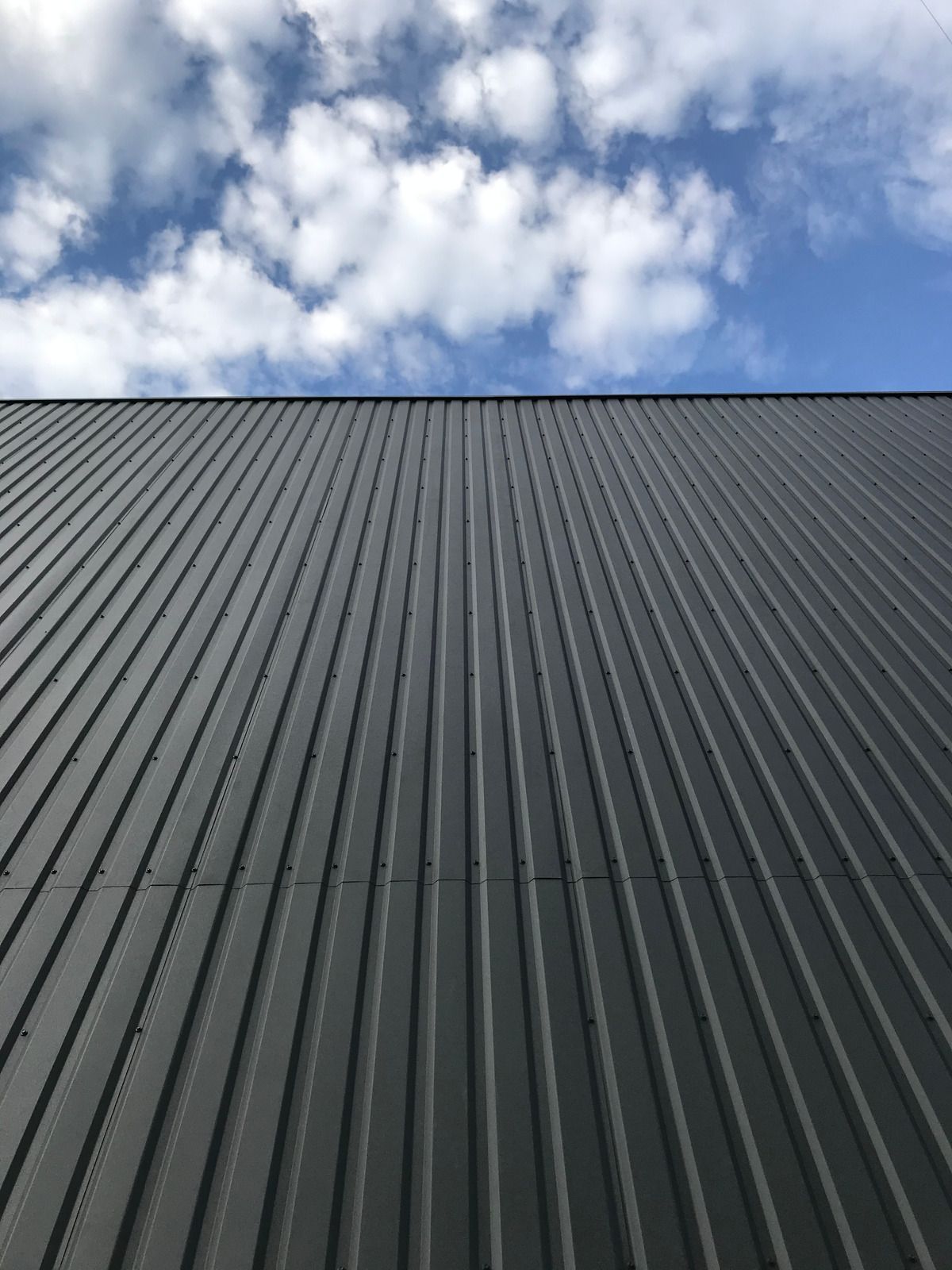 Dark corrugated roof beneath a partly cloudy blue sky