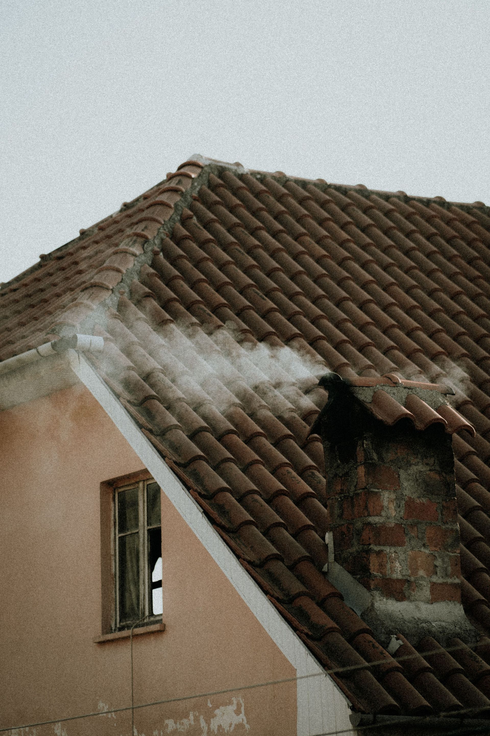 Damaged tiled house roof with smoke or steam rising near the eaves