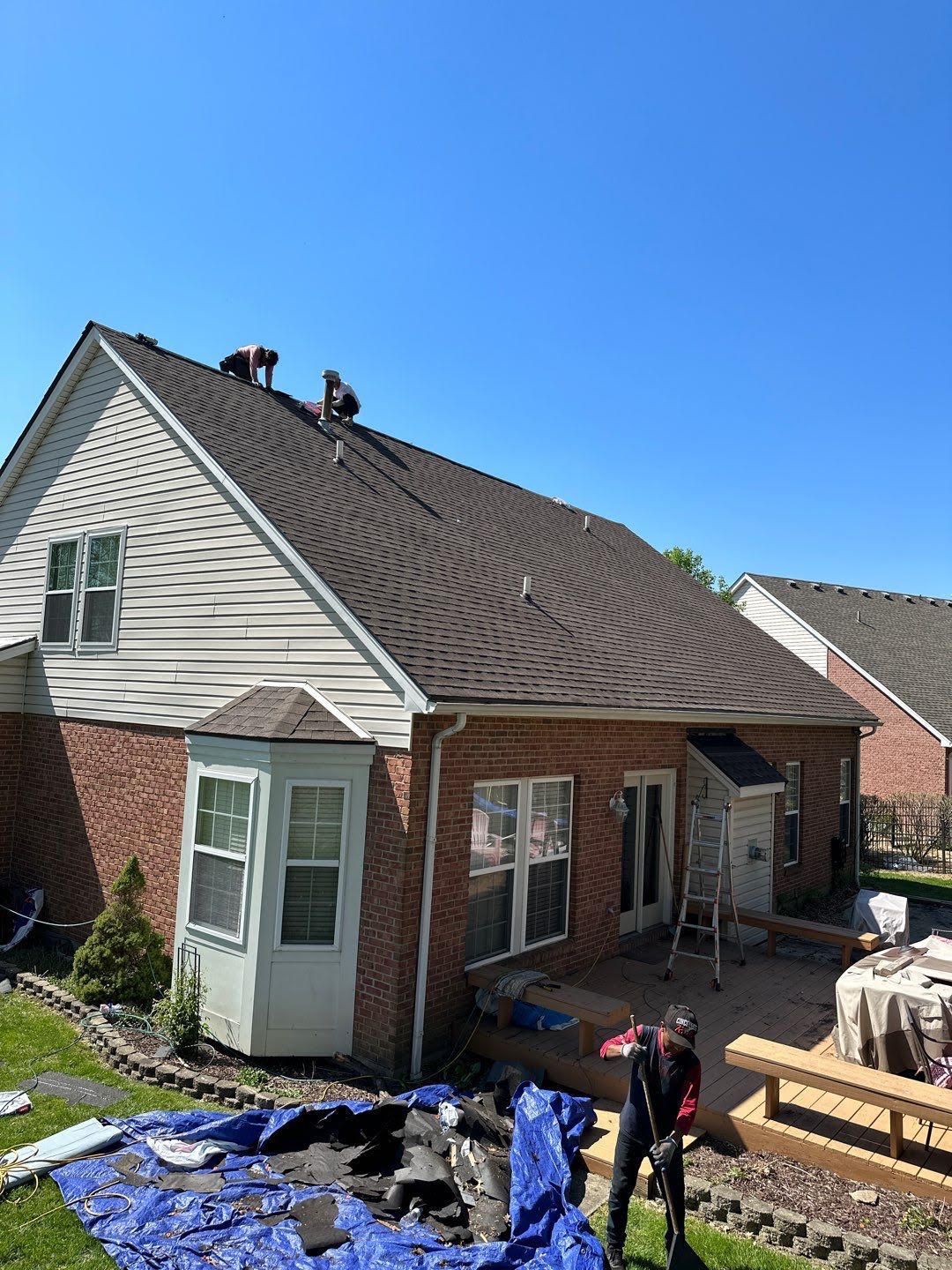 Roof replacement on a brick house with workers, tarps, and building materials in the yard