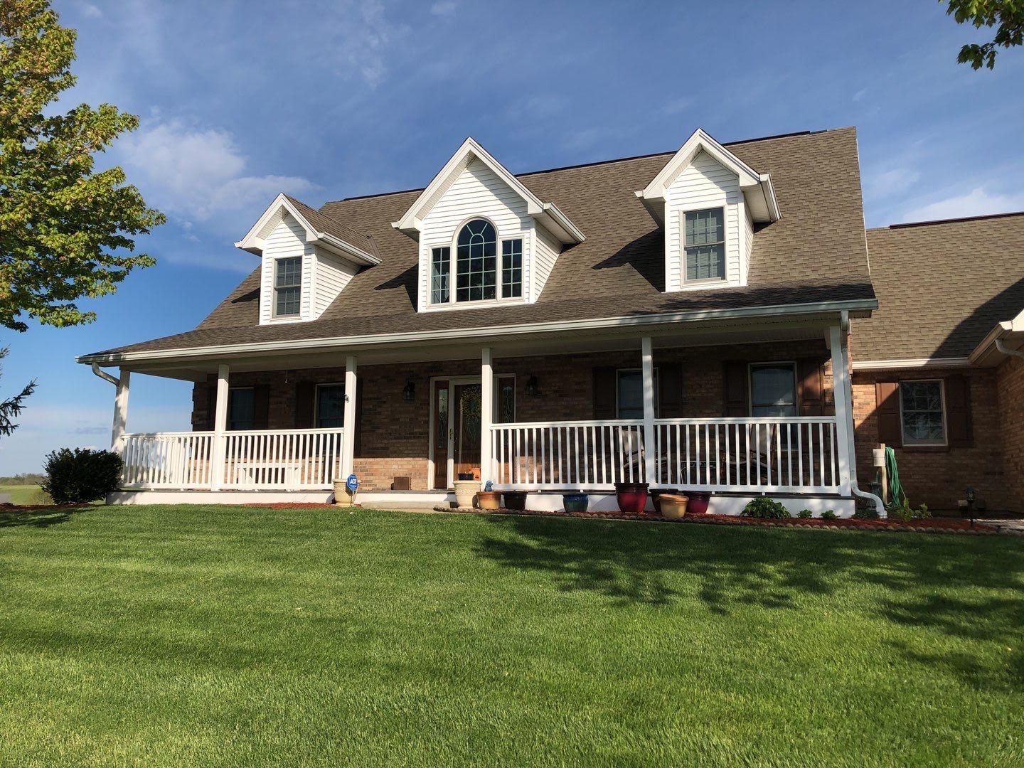 Brick house with white porch and dormers on a green lawn under a blue sky