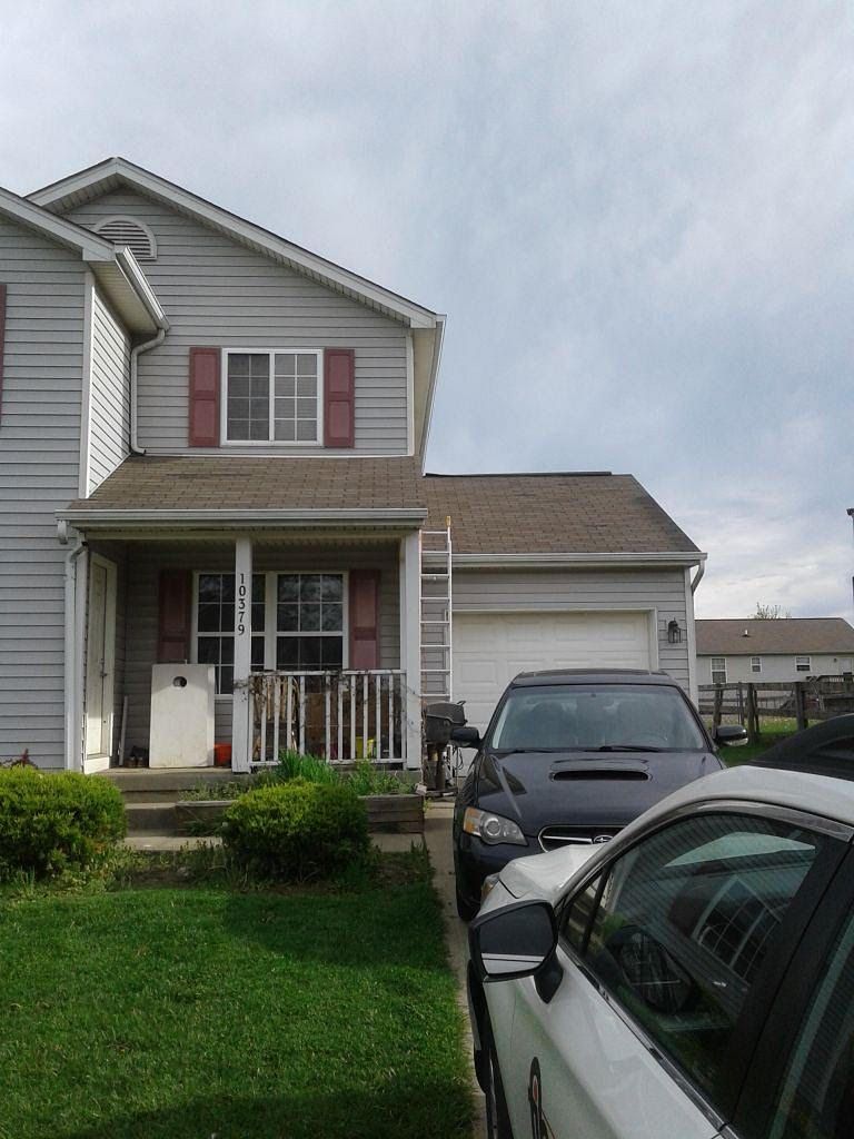 Suburban two-story house with a front porch, garage, and two parked cars on a cloudy day