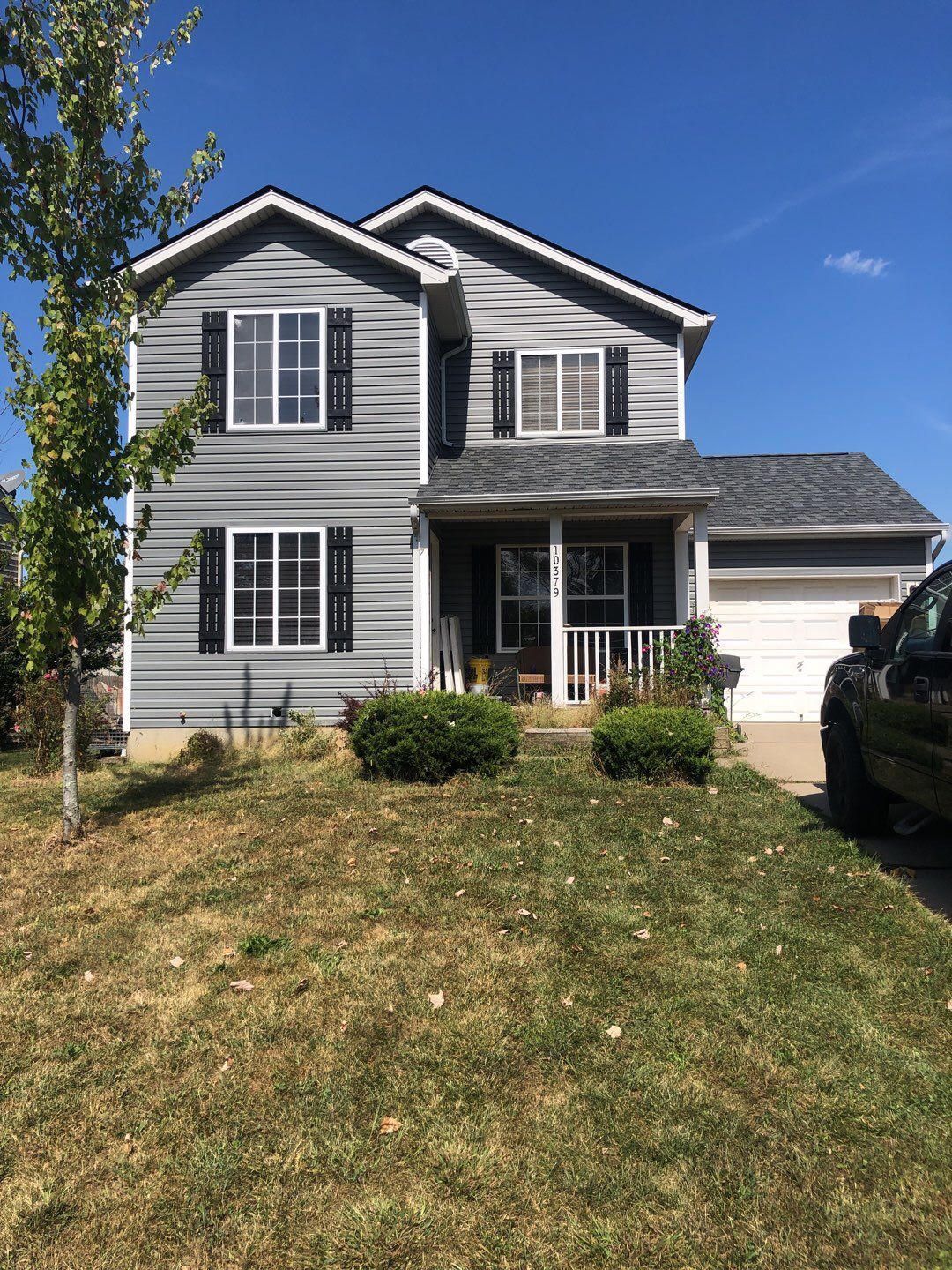 Two-story gray house with white trim, front porch, and driveway under a blue sky
