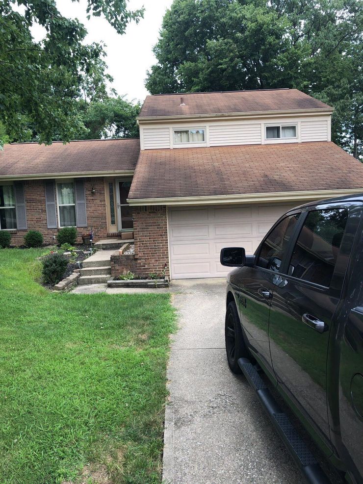 Suburban house with brick facade, front steps, driveway, and black truck parked beside the lawn.