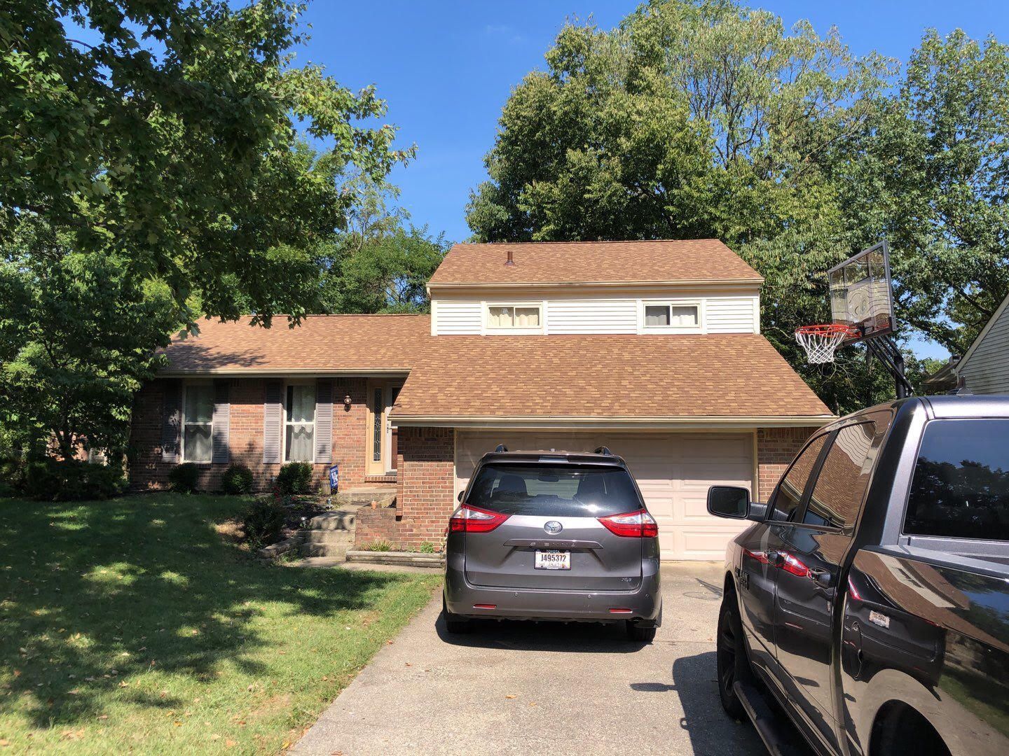 Suburban brick house with two parked SUVs in the driveway under a clear blue sky.