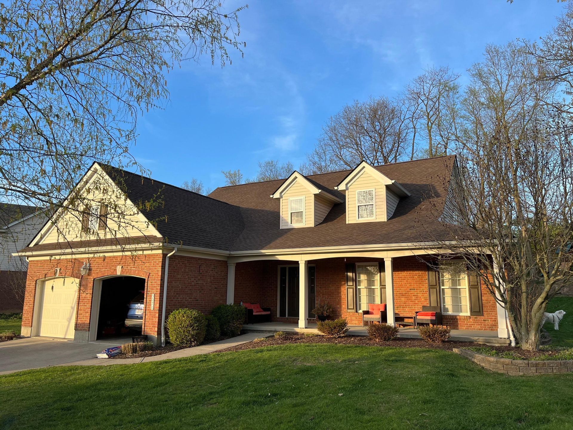 Brick suburban house with a two-car garage, front porch, and green lawn under a blue sky