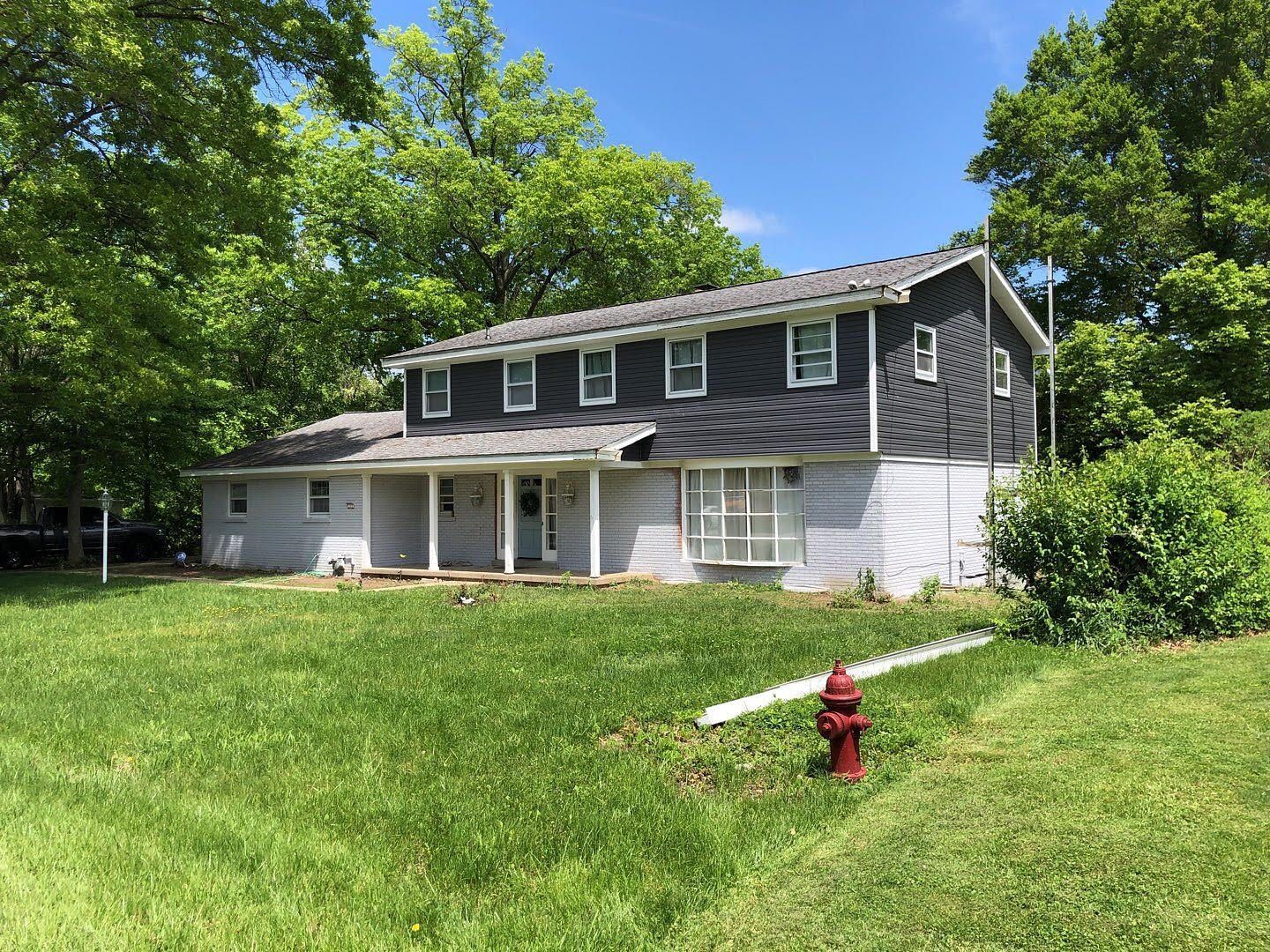 Two-story gray house with white trim and a red fire hydrant in a grassy yard under a blue sky