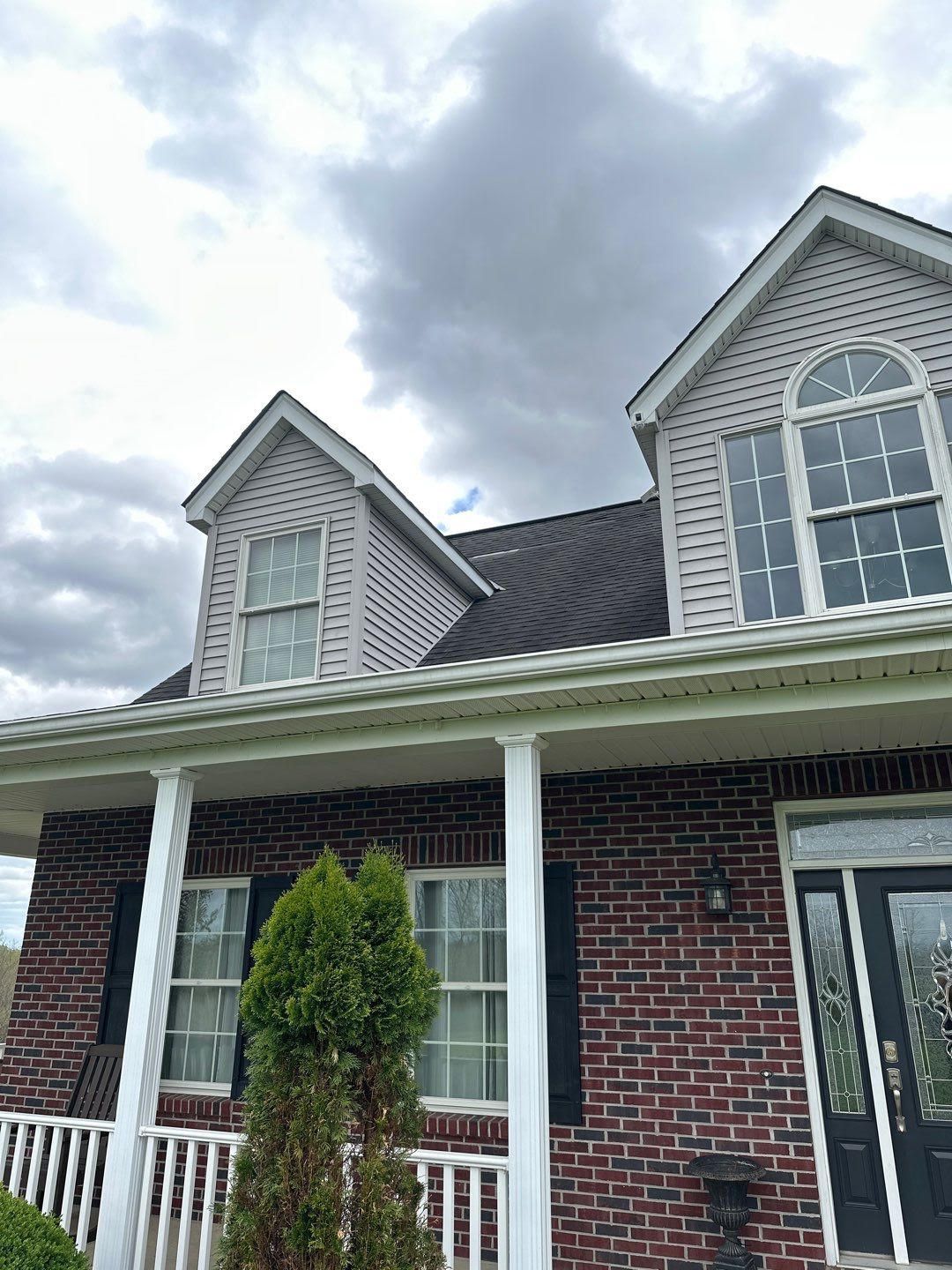 Brick house with white trim, front porch, and dormer windows under a cloudy sky