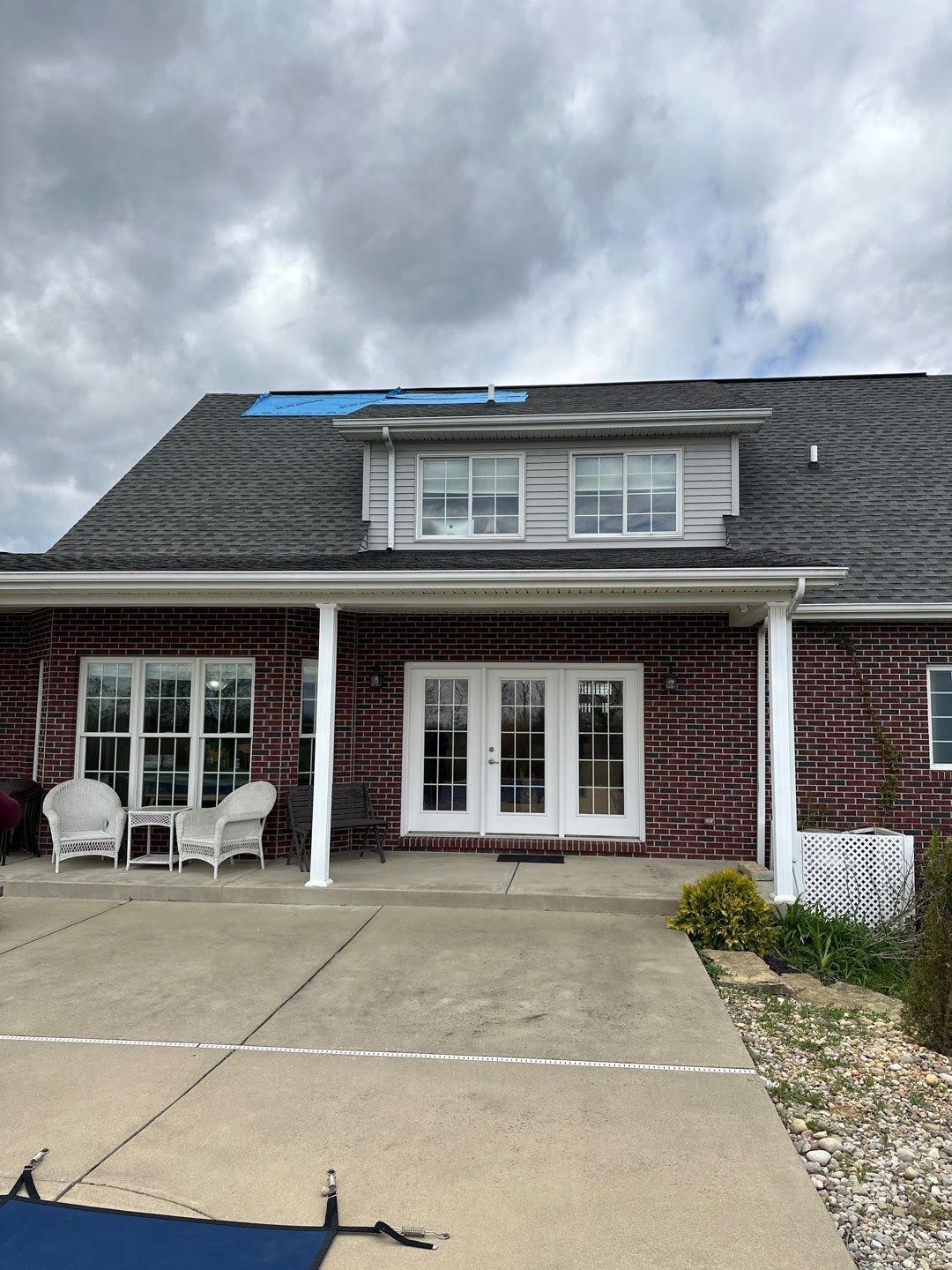 Brick house patio with white patio furniture, double doors, and a large concrete driveway under a cloudy sky