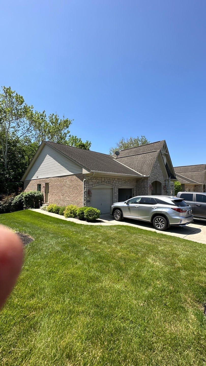 Suburban brick house with a silver SUV parked in the driveway under a clear blue sky