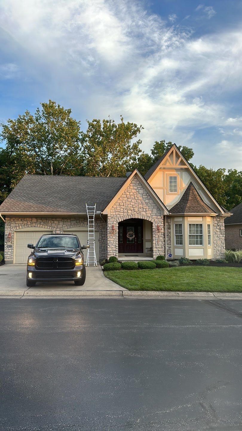 Suburban house with stone facade, arched entry, and a black car parked in the driveway at dusk