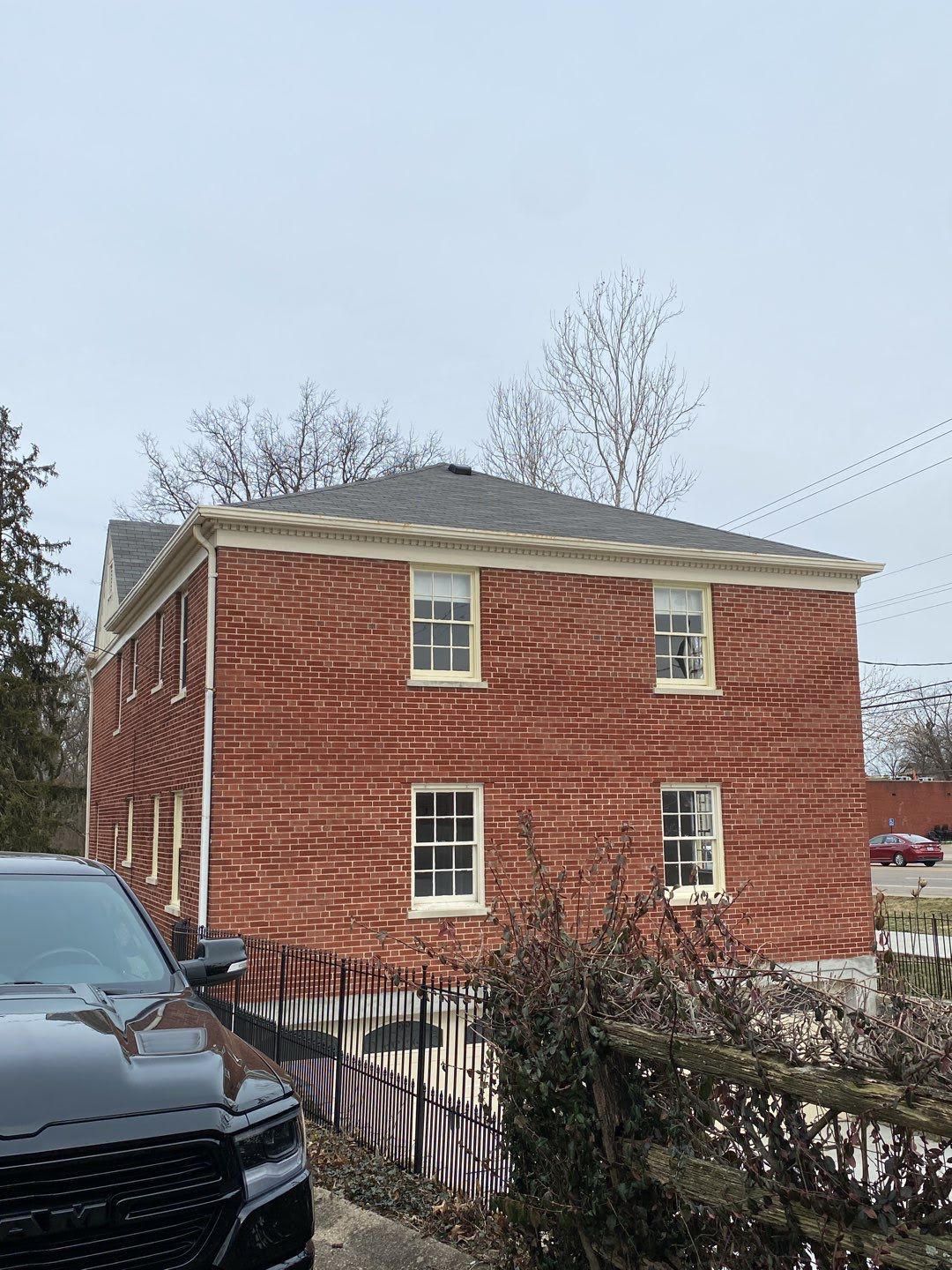 Two-story red brick house with white-trimmed windows and a black car in the foreground