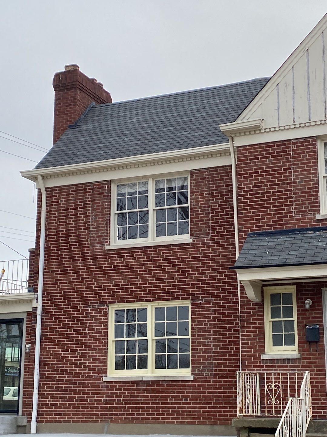 Red brick two-story house with white-trim windows and a chimney on a cloudy day