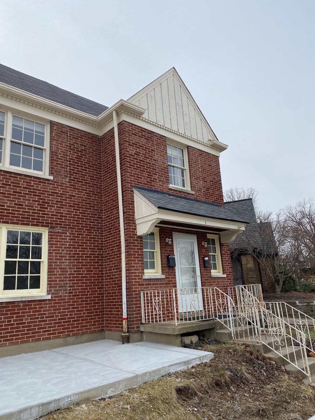 Red brick house with white trim, a small covered porch, and a concrete walkway in a wintery yard