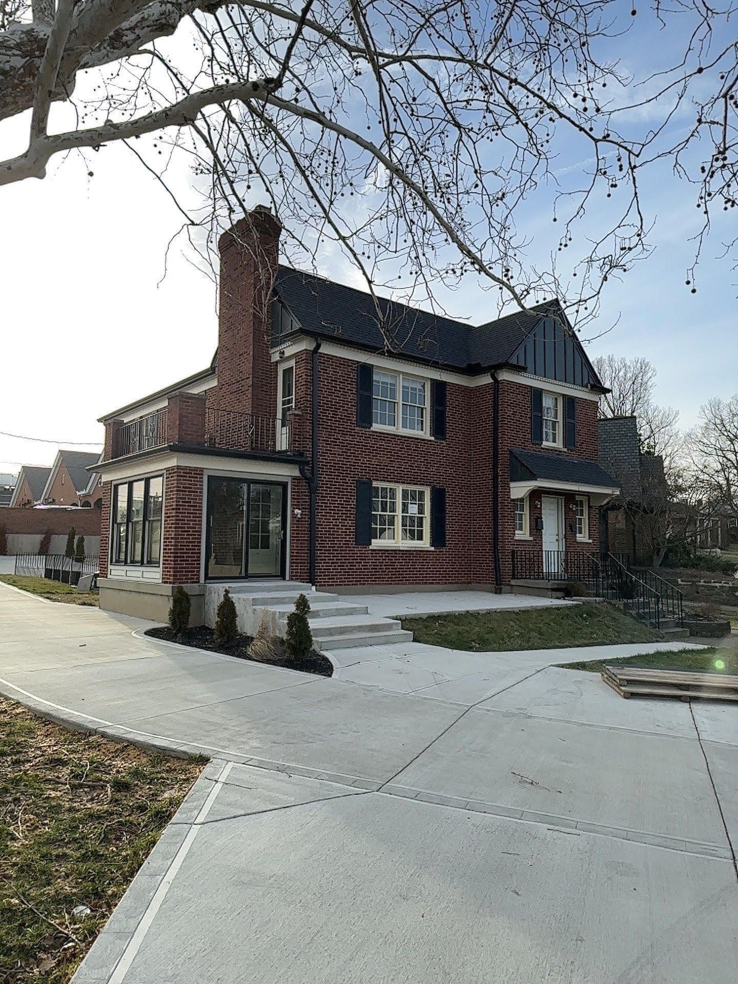 Red brick house with a chimney and white trim beside a curved concrete driveway in a suburban neighborhood
