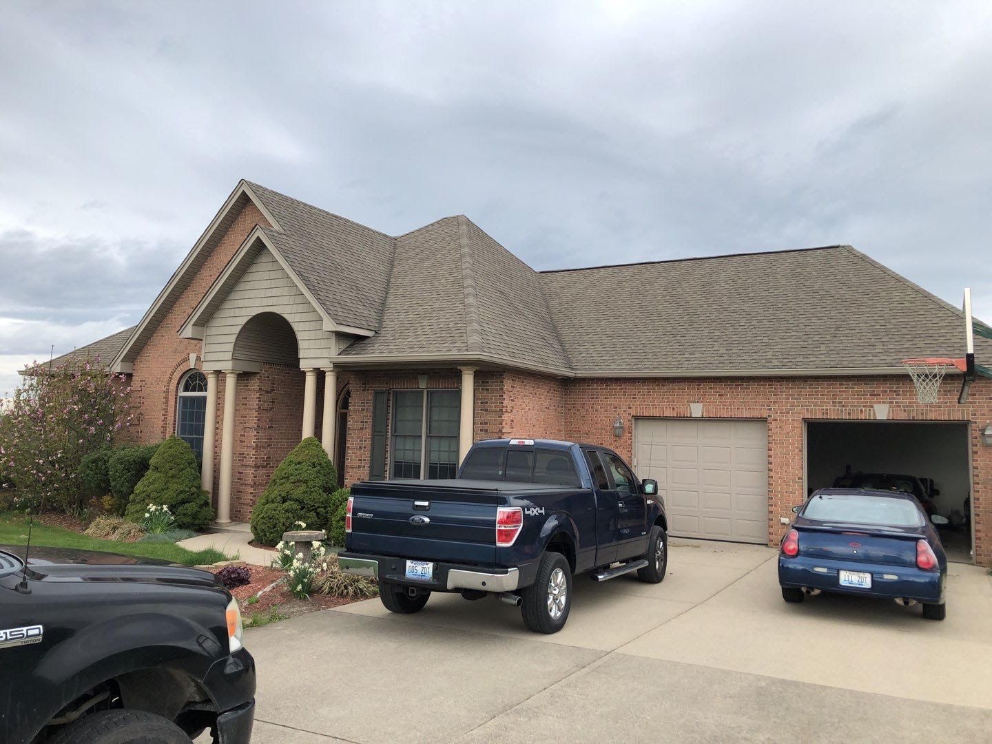 Brick suburban house with two cars parked in the driveway and a pickup truck near the garage.