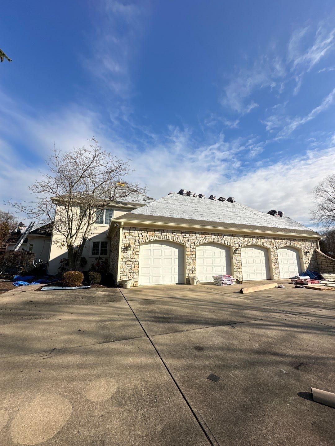Suburban house with two white garage doors under a blue, cloudy sky, viewed from a driveway