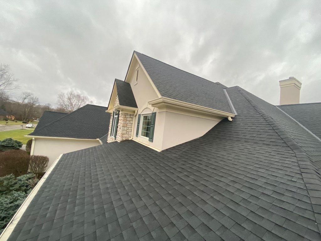 Slate-gray roof on a house with dormer windows under a cloudy sky