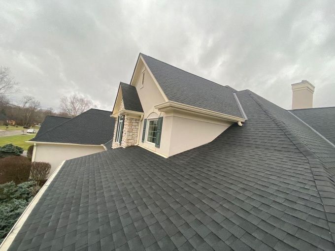 Steep gray shingle roof on a beige house under a cloudy sky