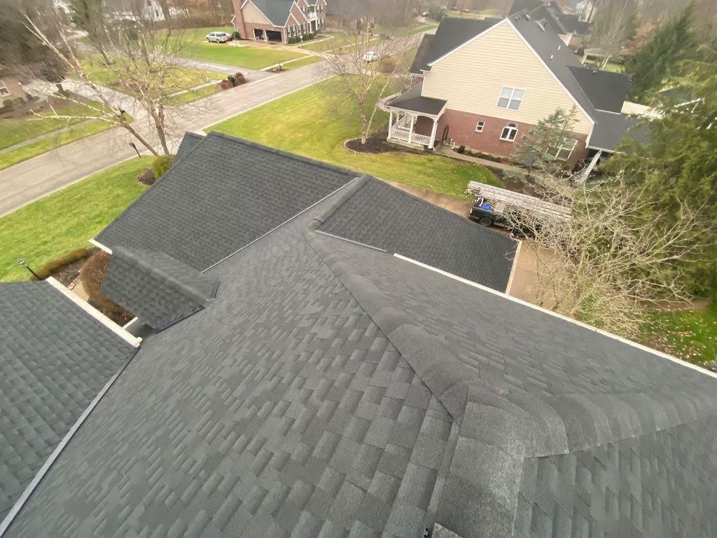 Aerial view of black shingled rooftops in a suburban neighborhood with trees and houses.