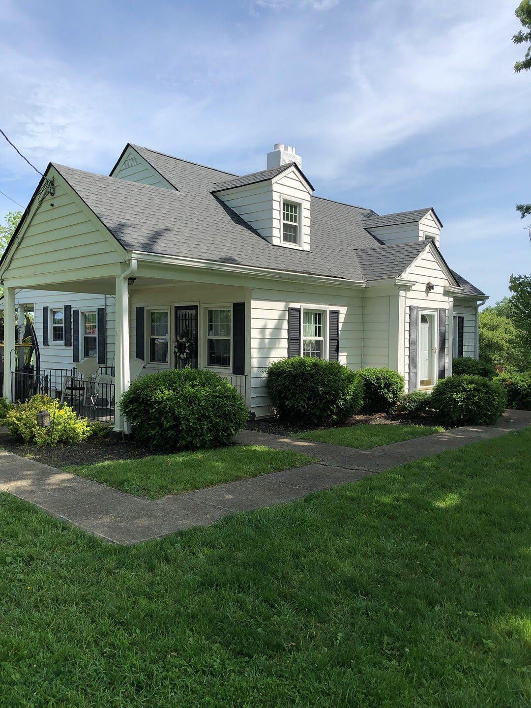 Small white house with gray roof, front porch, and green lawn under a blue sky