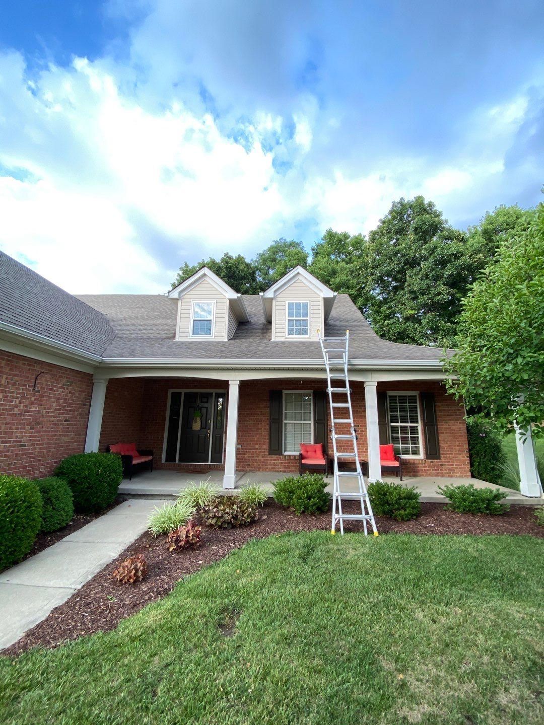 Brick house with white dormer windows and a ladder leaning to the roof under a blue sky