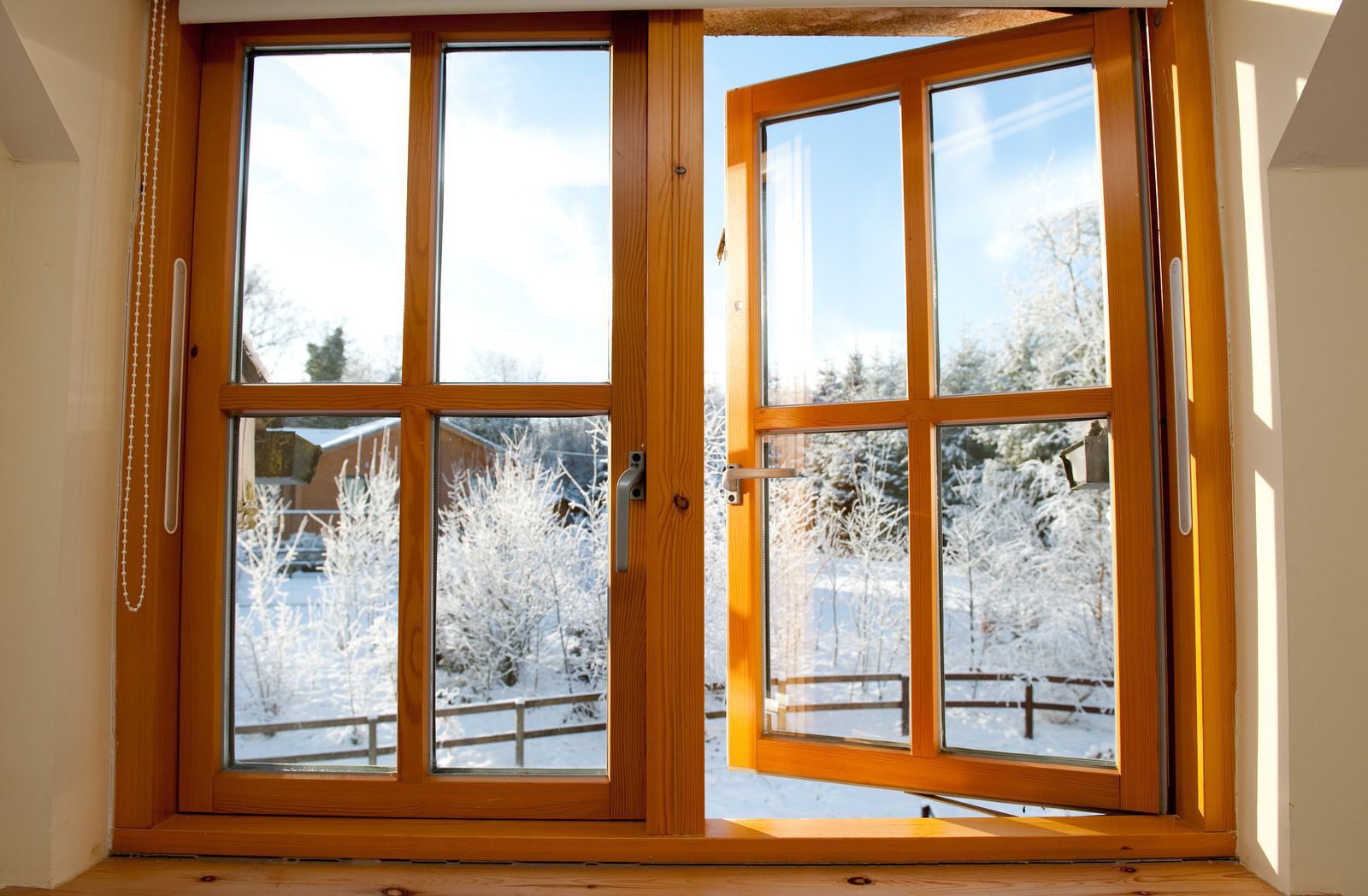 Wooden window frame with open panes overlooking a snowy landscape and bright winter light