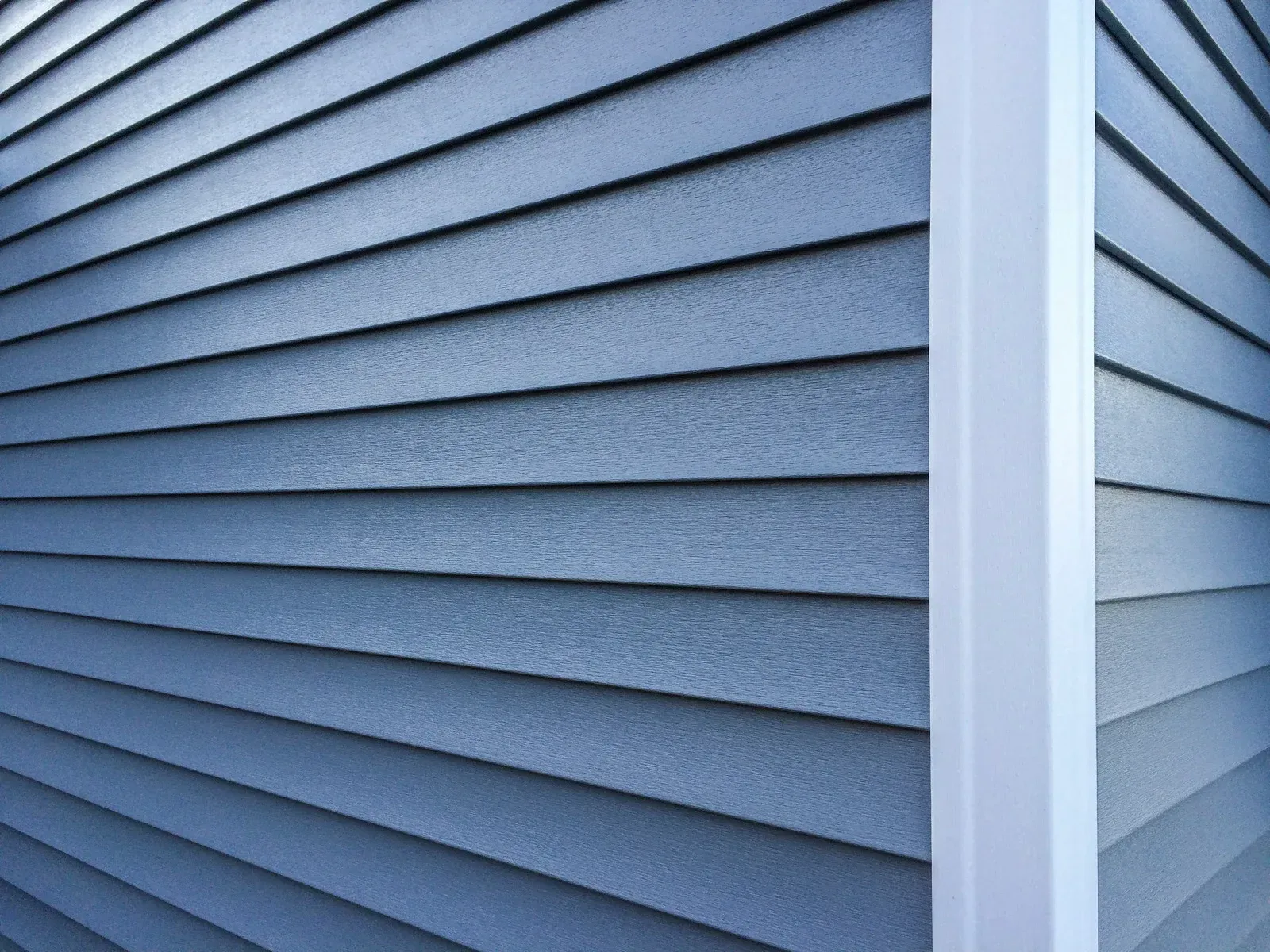 Blue vinyl siding on a house exterior with white trim at the corner