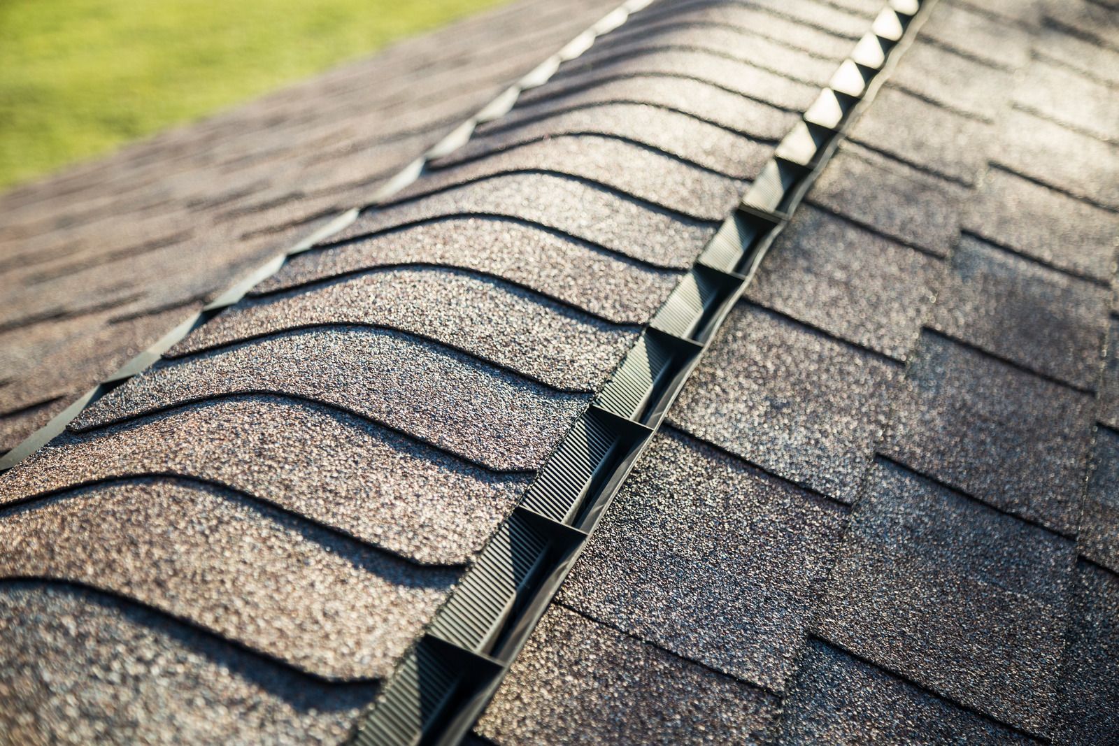 Close-up of a damaged shingle roof with a gap along the ridge and split vent strip